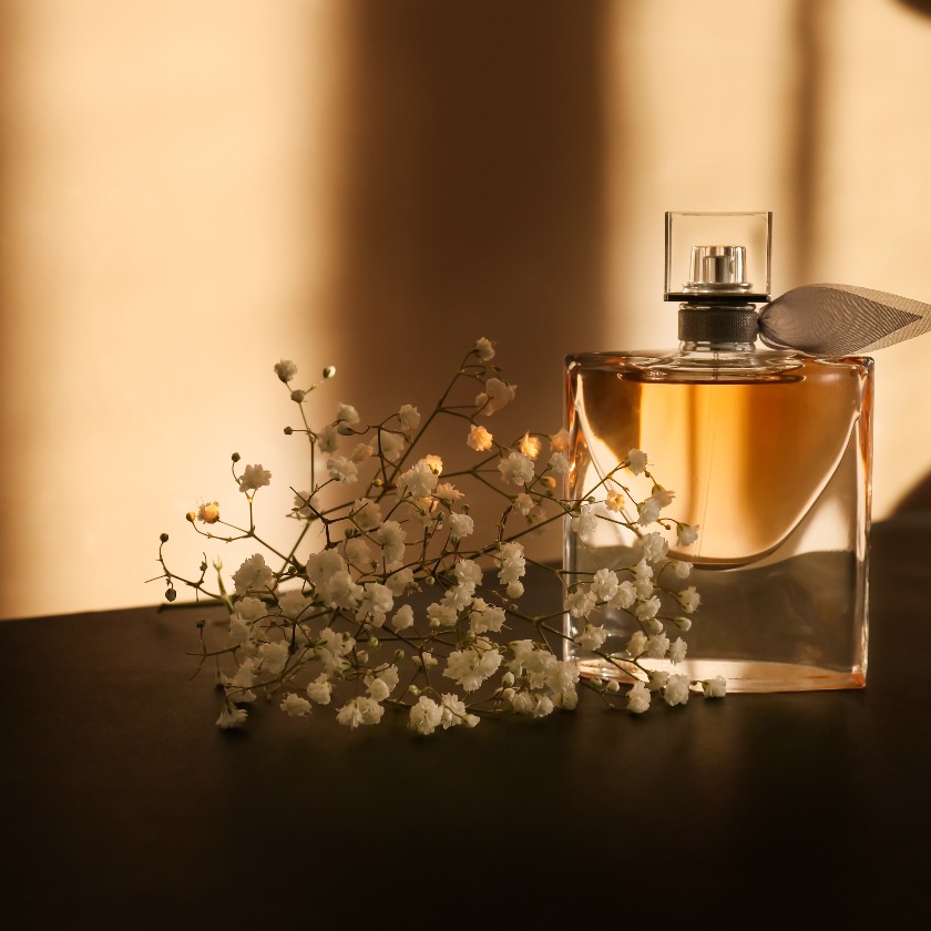 Transparente Parfümflasche mit wunderschönen Blumen auf einem dunklen Etikett